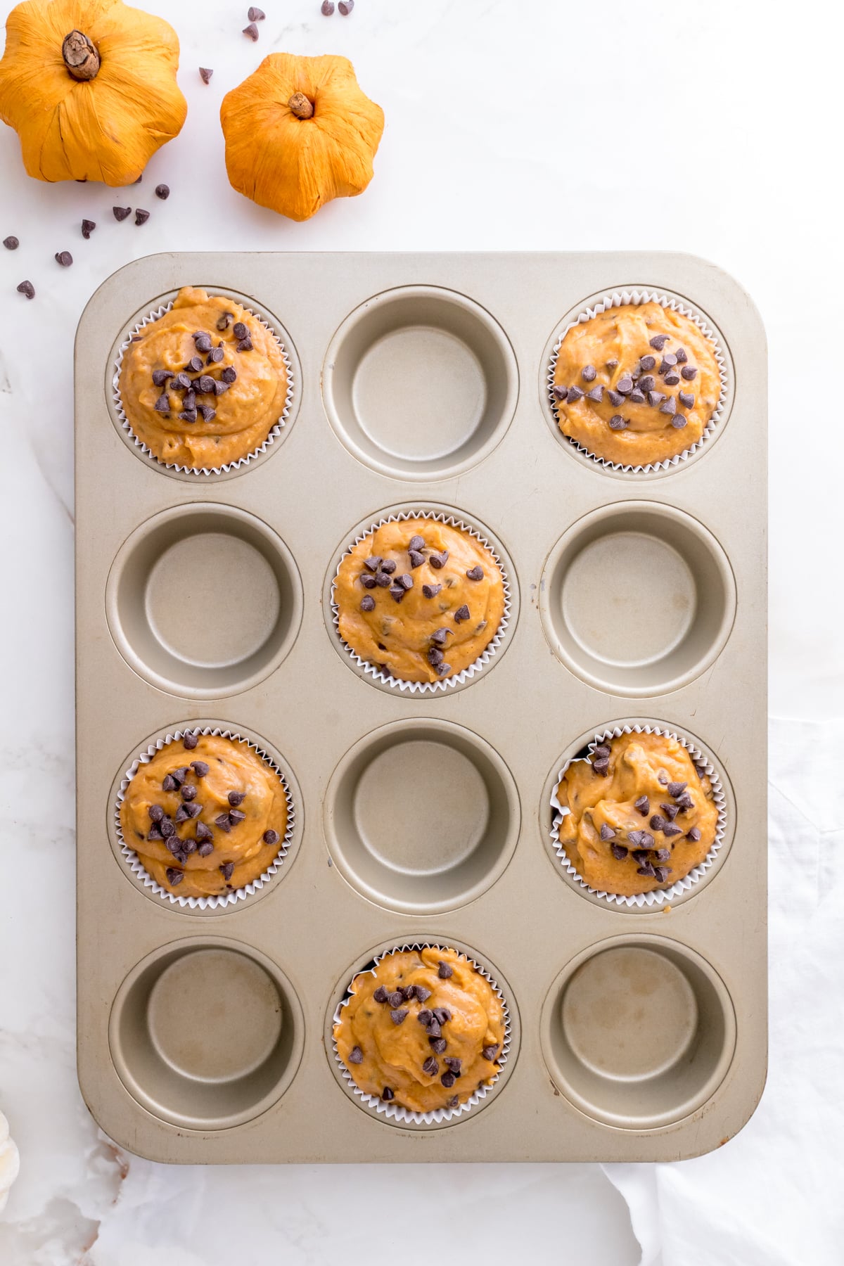 gold muffin pan filled with pumpkin chocolate chip muffin batter.