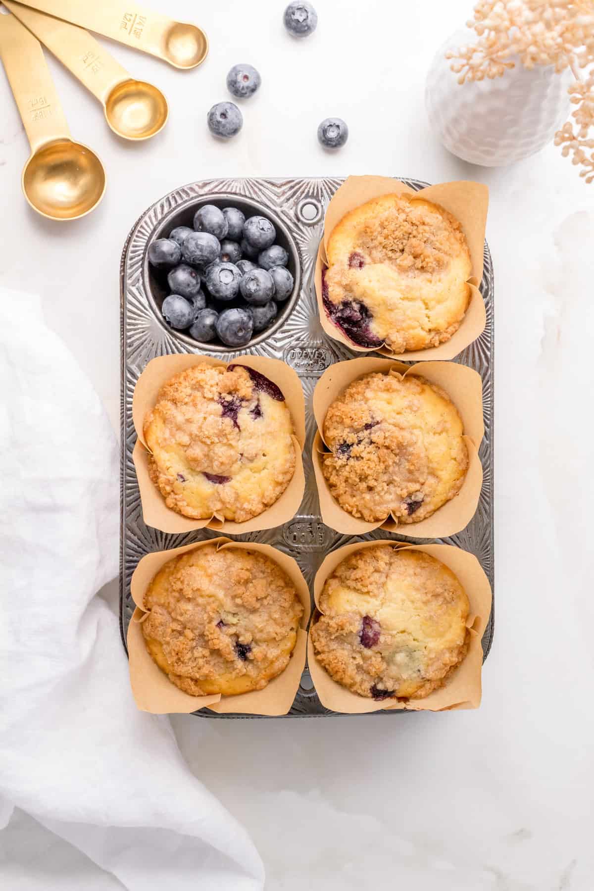 pan of discard blueberry muffins with blueberries and gold measuring spoons.