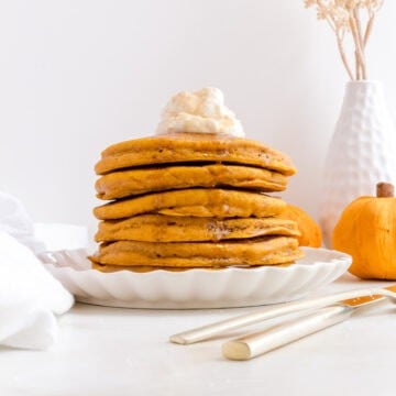 a stack of pumpkin spice pancakes with homemade whipped cream and warm maple syrup.