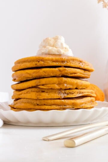 a stack of pumpkin spice pancakes with homemade whipped cream and warm maple syrup.