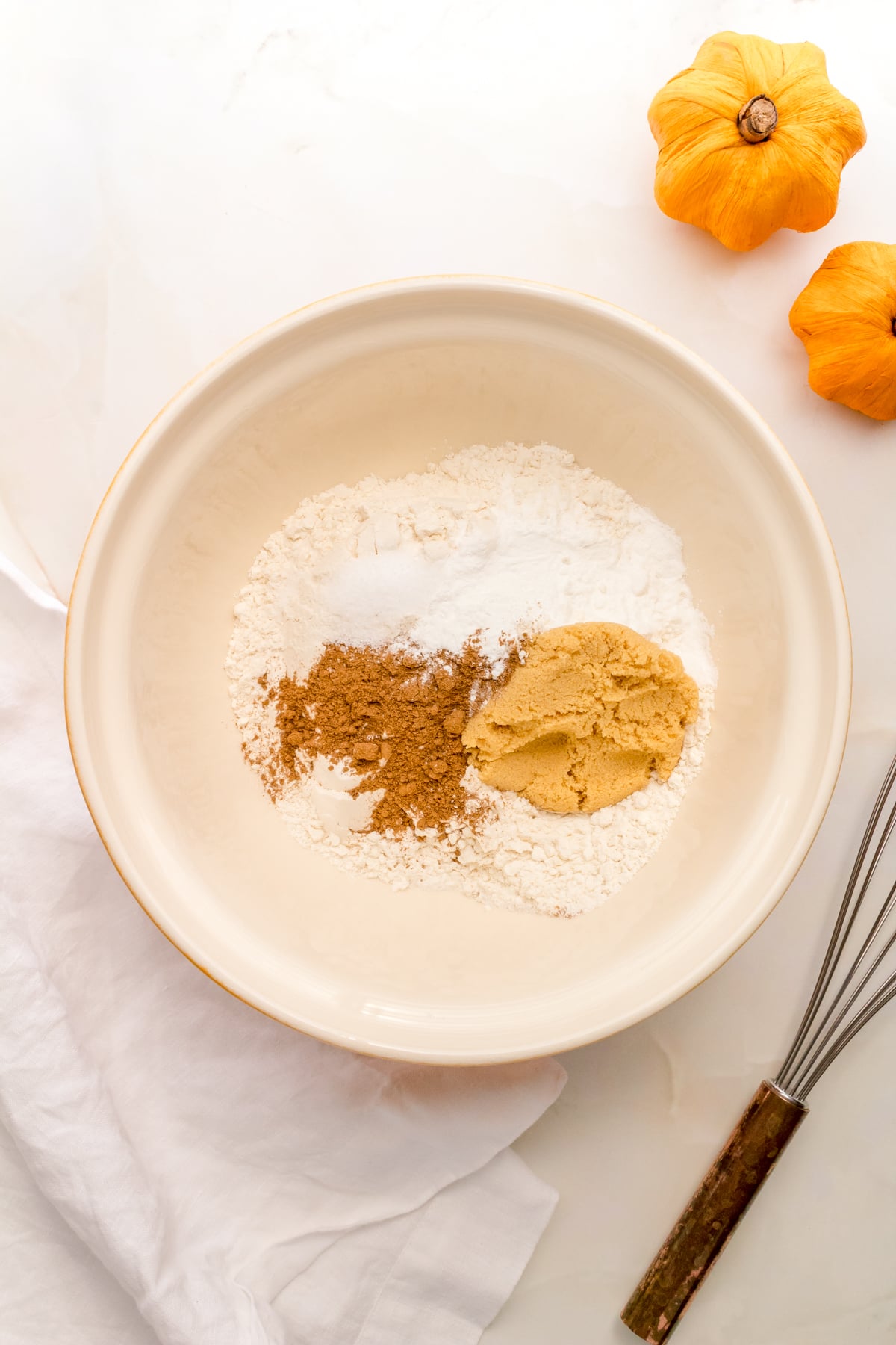 a white mixing bowl filled with dry ingredients and pumpkin spice for pancakes. 