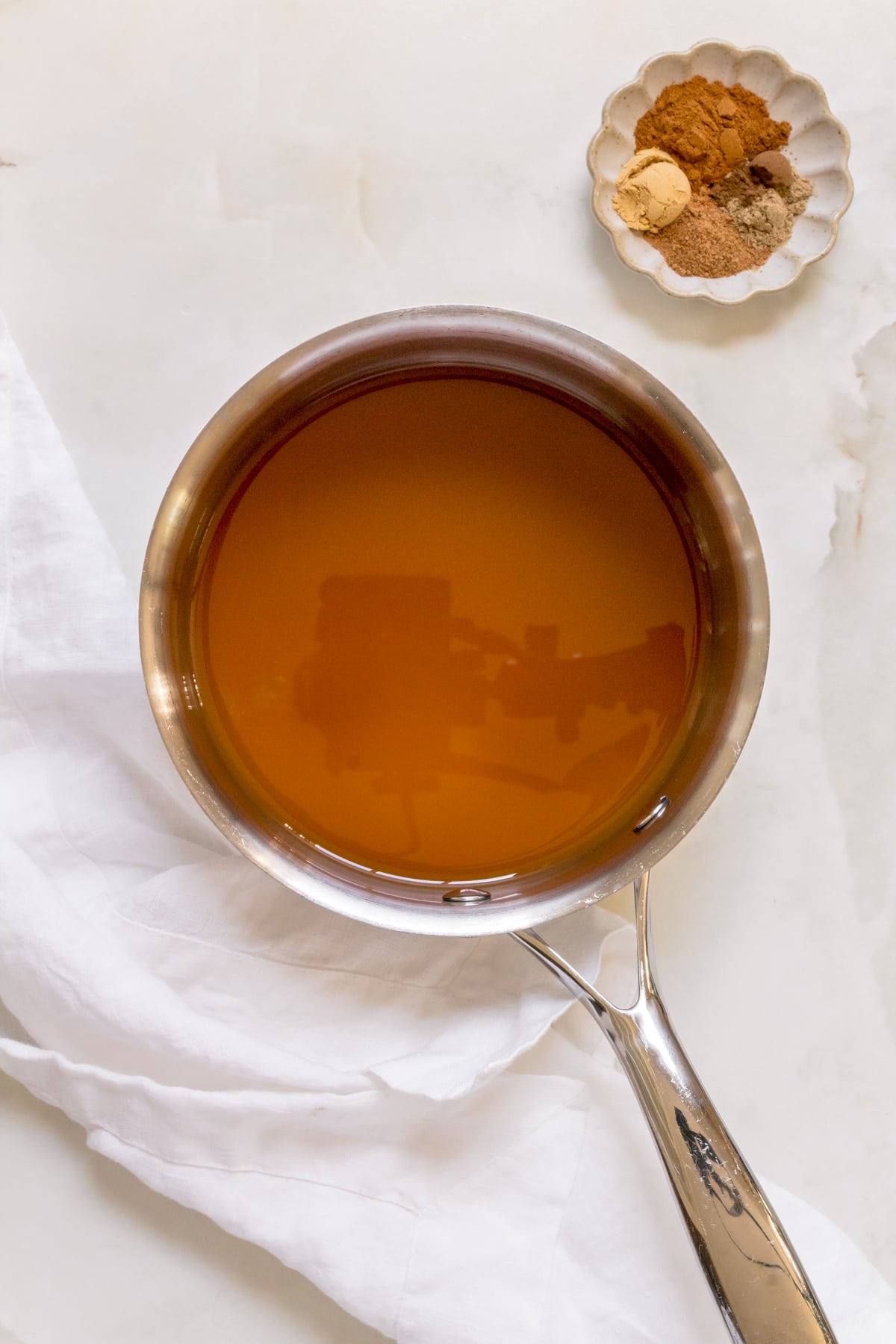 apple cider in a small silver saucepan with small bowl of cinnamon.