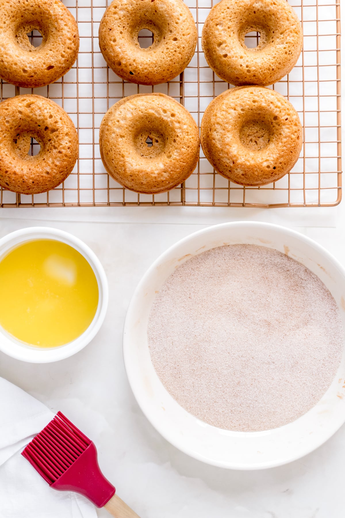 apple cider donuts on cooling rack with melted butter and bowl of cinnamon and sugar.