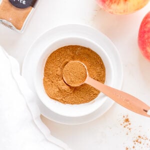 a white bowl filled with apple pie spice with a copper measuring spoon.