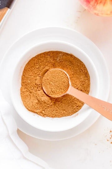 a white bowl filled with apple pie spice with a copper measuring spoon.