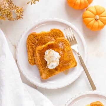 two slices of pumpkin French toast on white plates with maple syrup.