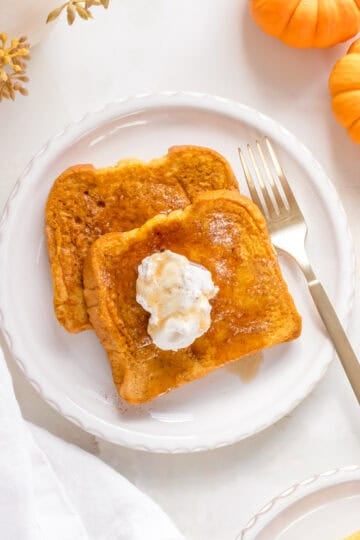 two slices of pumpkin French toast on white plates with maple syrup.